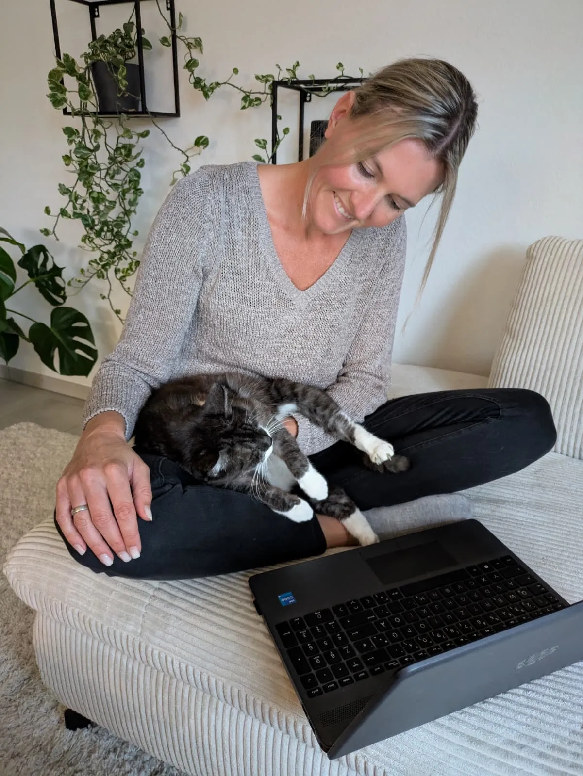 Christine sitzt lachend mit ihrer Katze und dem Laptop auf dem Sofa